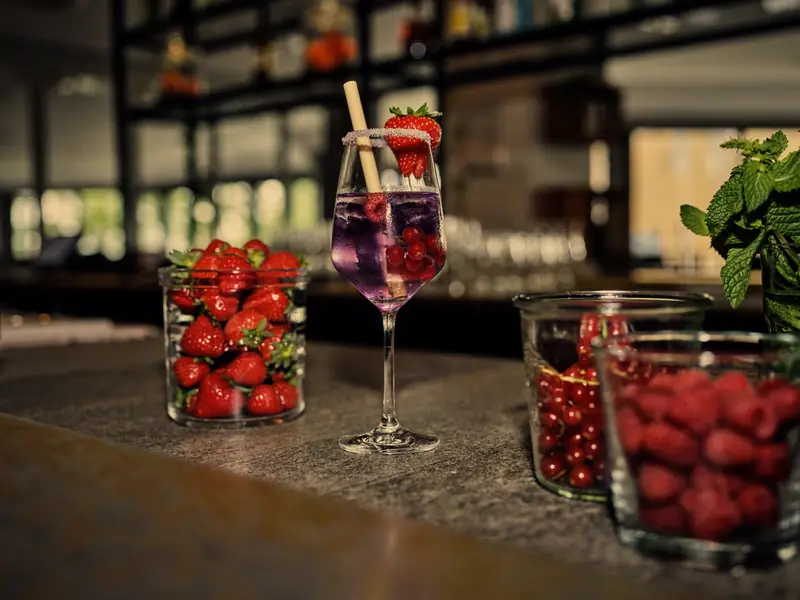 Beeren-Spritz auf dem Steintresen, daneben Gläser mit Erdbeeren und Himbeeren